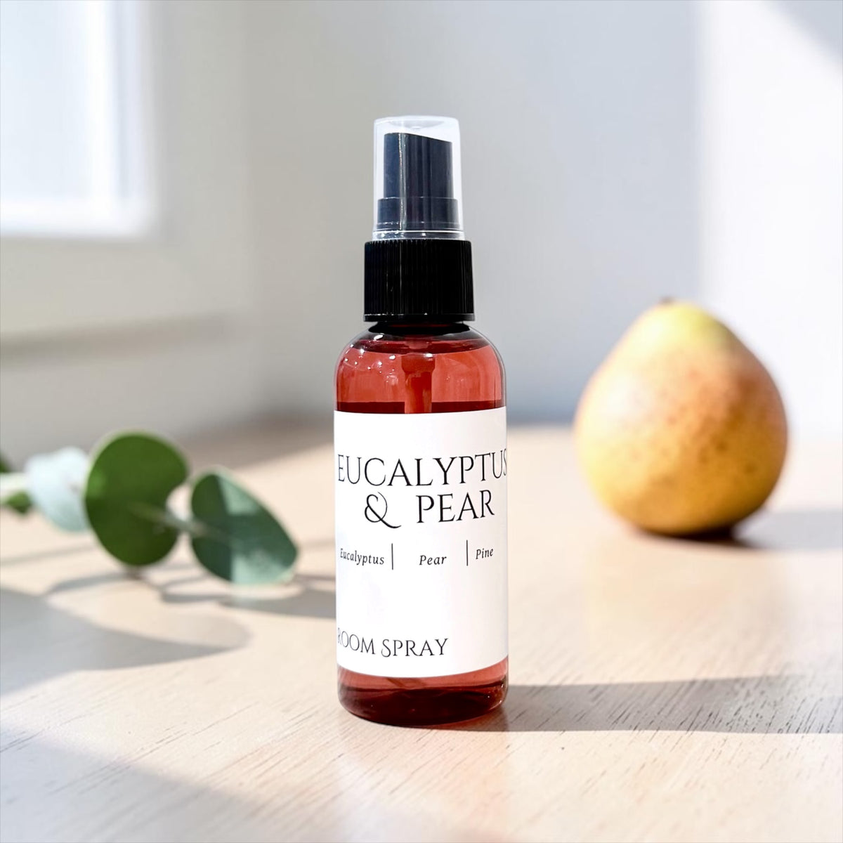 Eucalyptus & Pear room spray bottle with eucalyptus leaves and a pear on a wood table