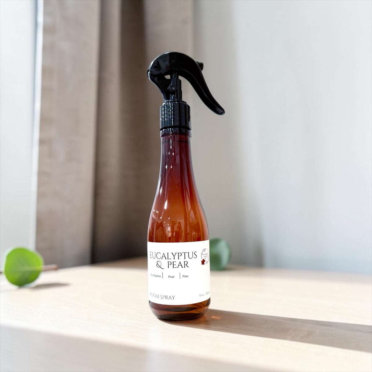 Eucalyptus & Pear room spray bottle on a wood table with greenery