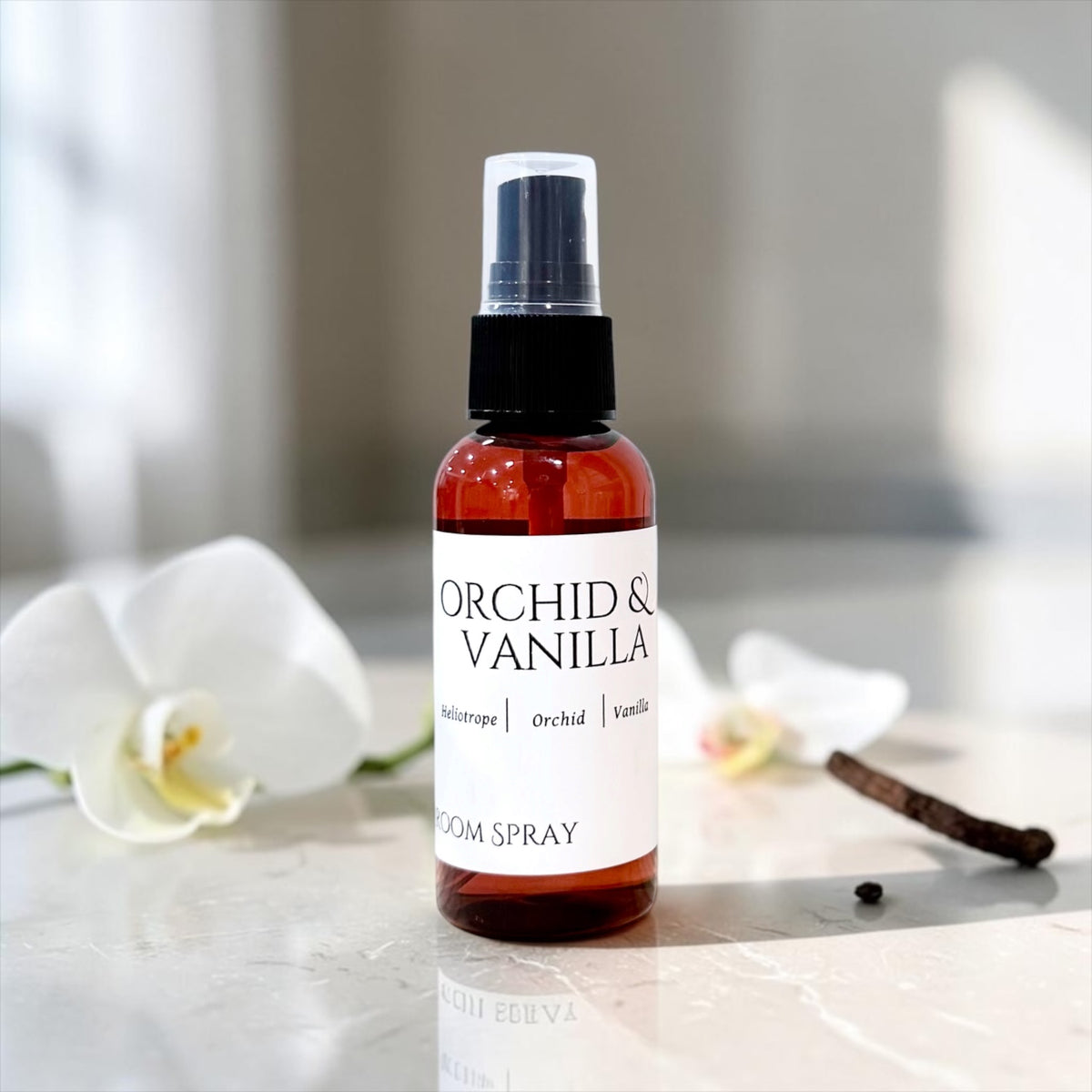 Orchid & Vanilla room spray bottle with white orchids and a vanilla bean on marble
