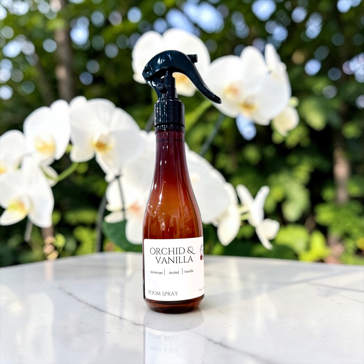 Orchid & Vanilla room spray bottle with white orchid flowers outdoors