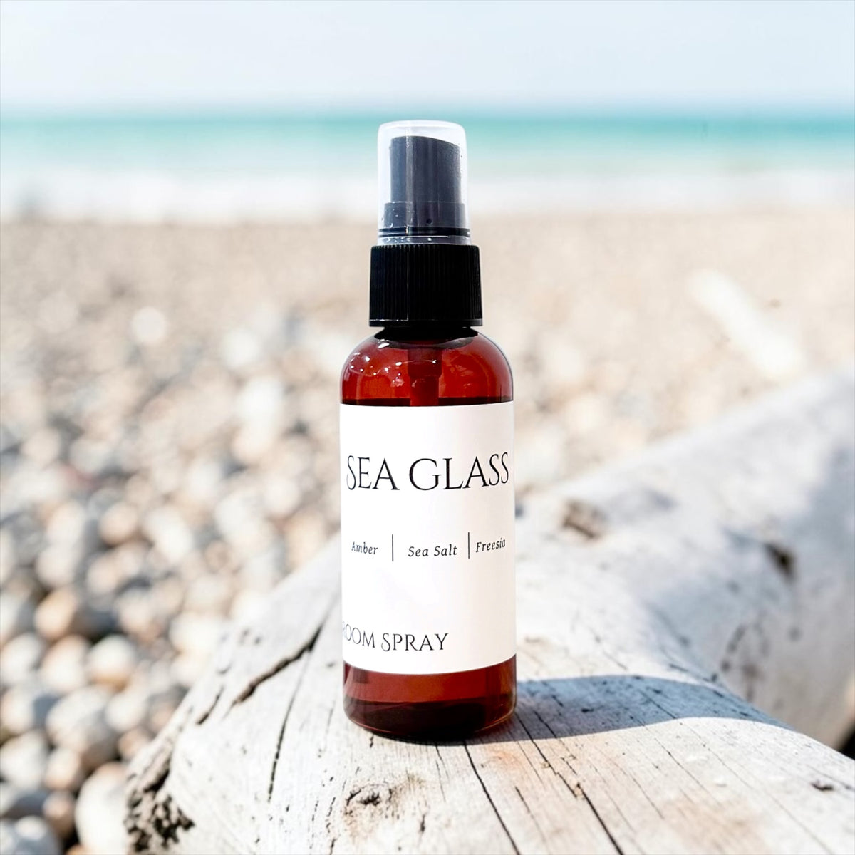 Sea Glass room spray bottle on sand with the ocean in the background
