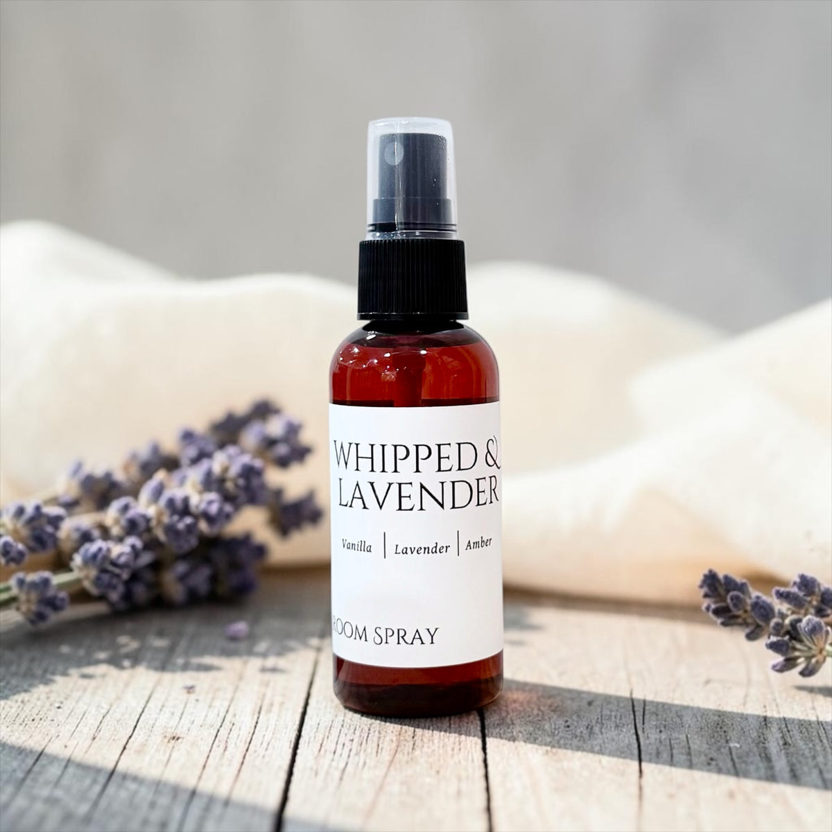 Whipped Lavender room spray bottle with dried lavender bundles on a wood table