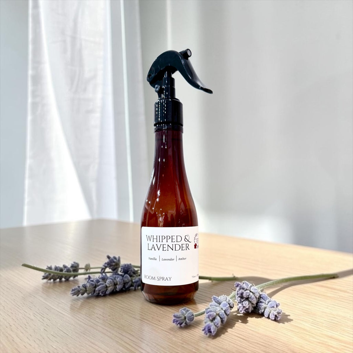 Whipped Lavender room spray bottle on a wood table by a sheer curtain